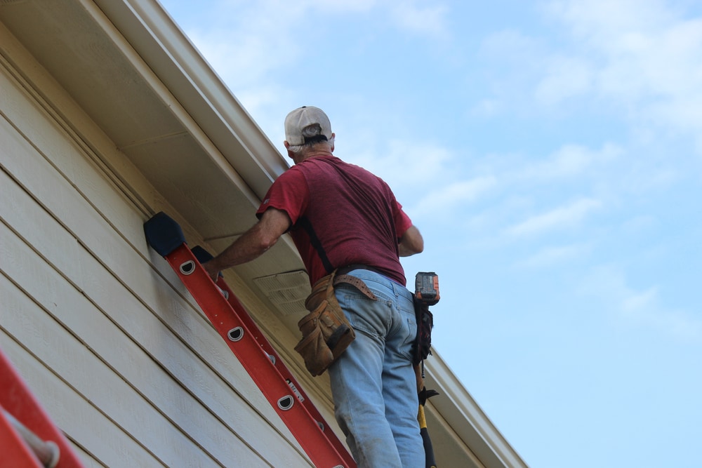 Contractor Installing Gutter System On A Two Story Residential House