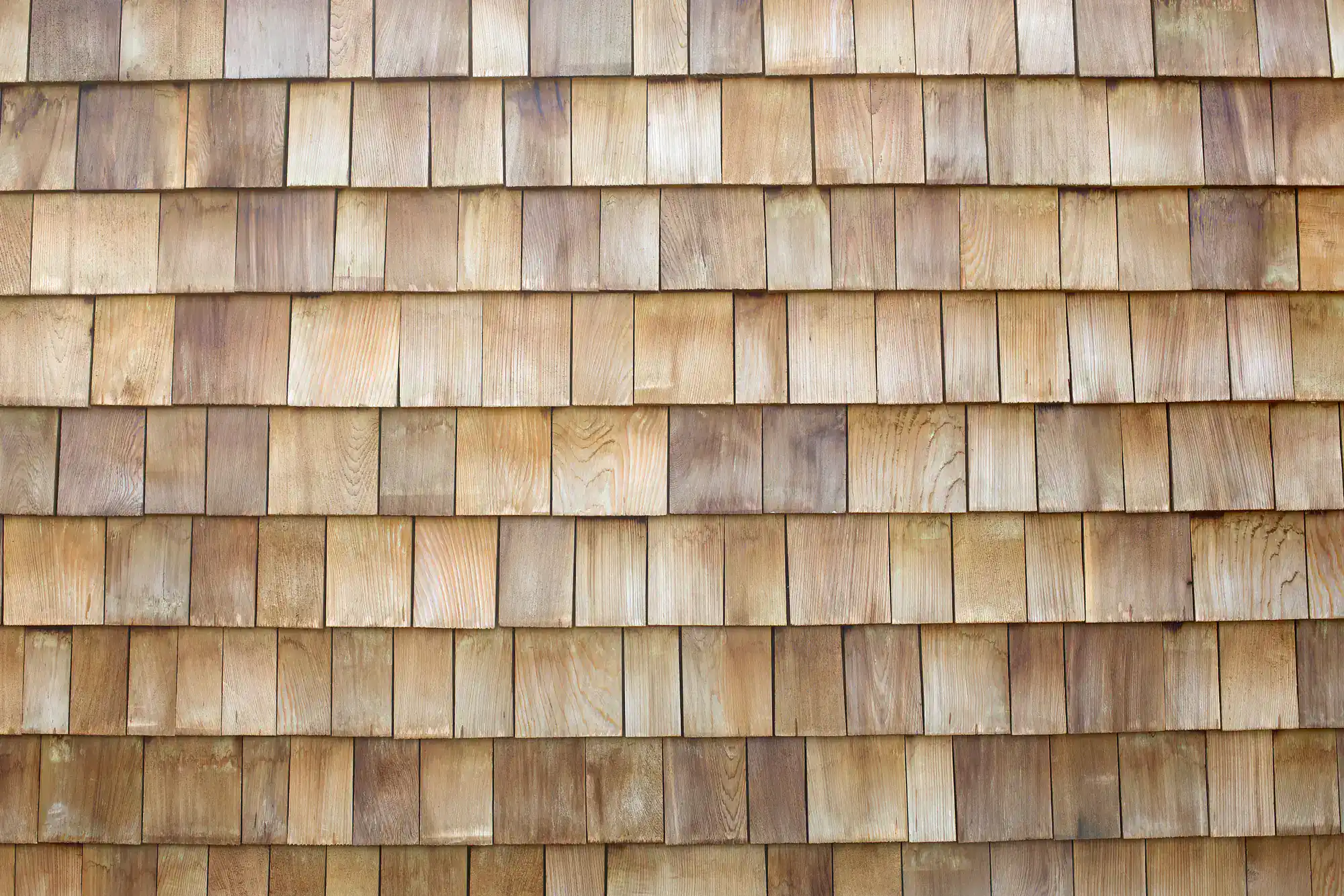 A close-up view of overlapping wooden shingles arranged in neat, horizontal rows, displaying natural wood grain and various light brown tones.