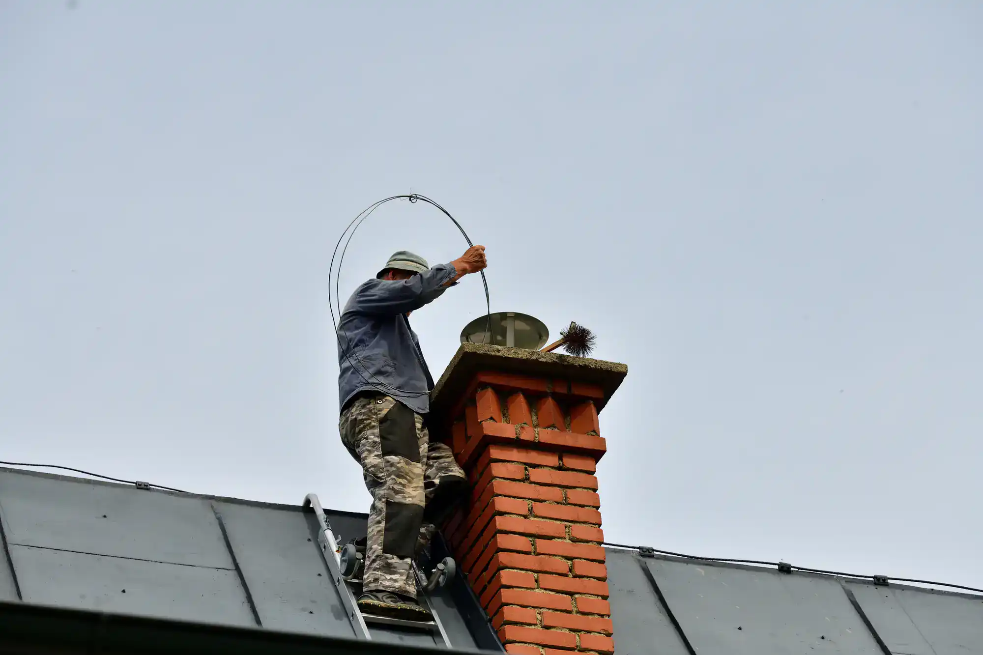 Chimney sweep performing maintenance on a rooftop in Suffolk County, NY, with SkyLuxe Construction truck visible in the background